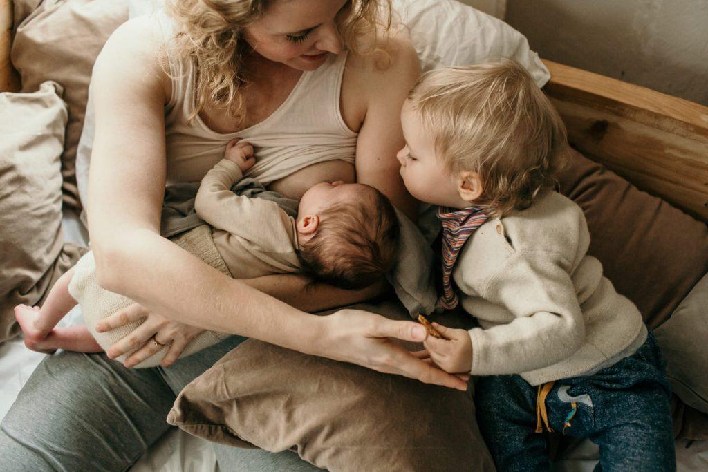 Mutter stillt Baby im Wochenbett erstes Kind schaut zu