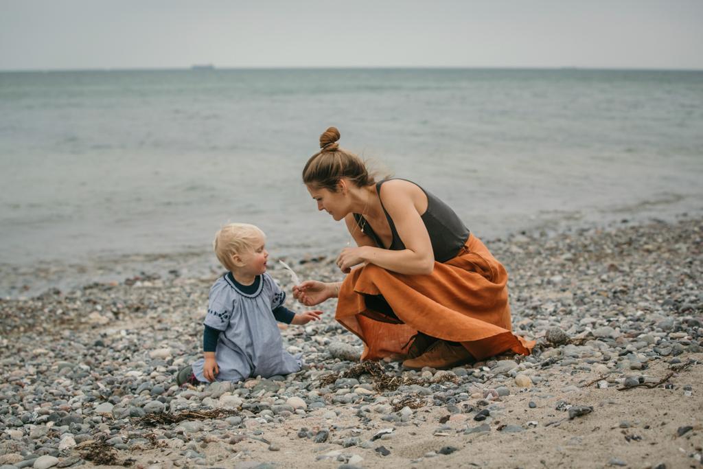Mutter und Tochter sammeln Muscheln am Strand, während die Mutte eine Feder in der Hand hält