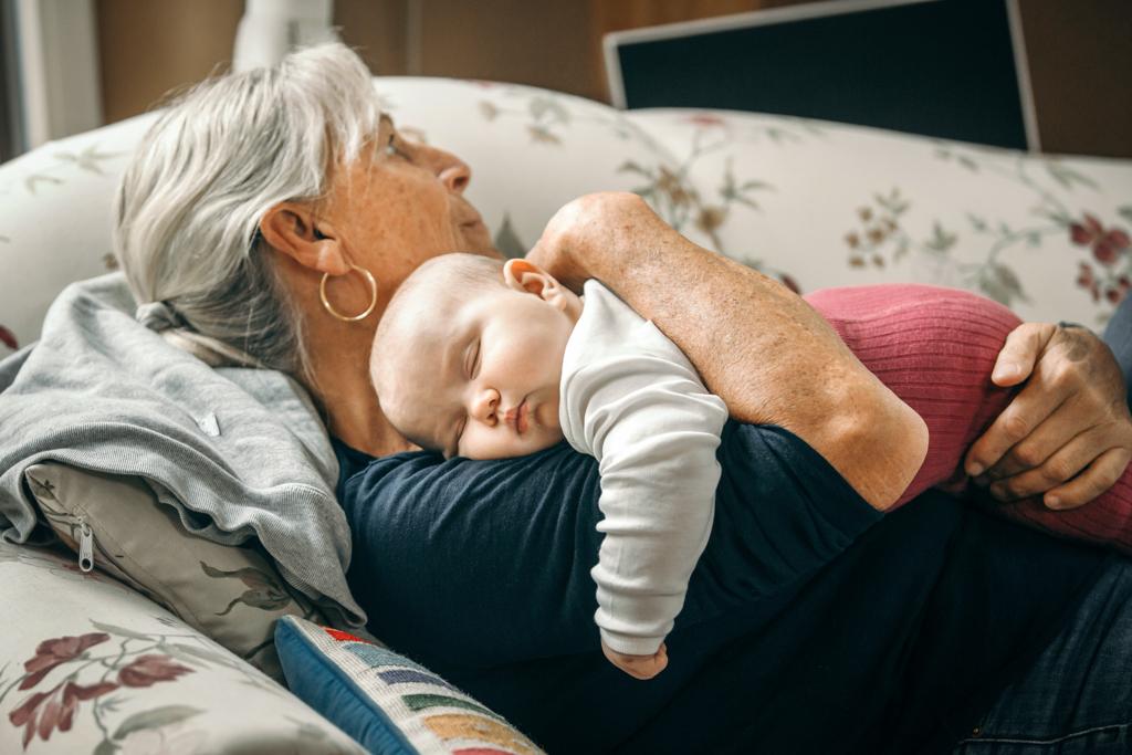 Oma hält schlafendes Enkelkind auf dem Sofa