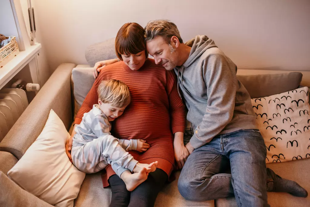 Babybauchfotos - Mama mit Babybauch, kleinem Sohn und Papa kuscheln liebevoll auf der Couch.