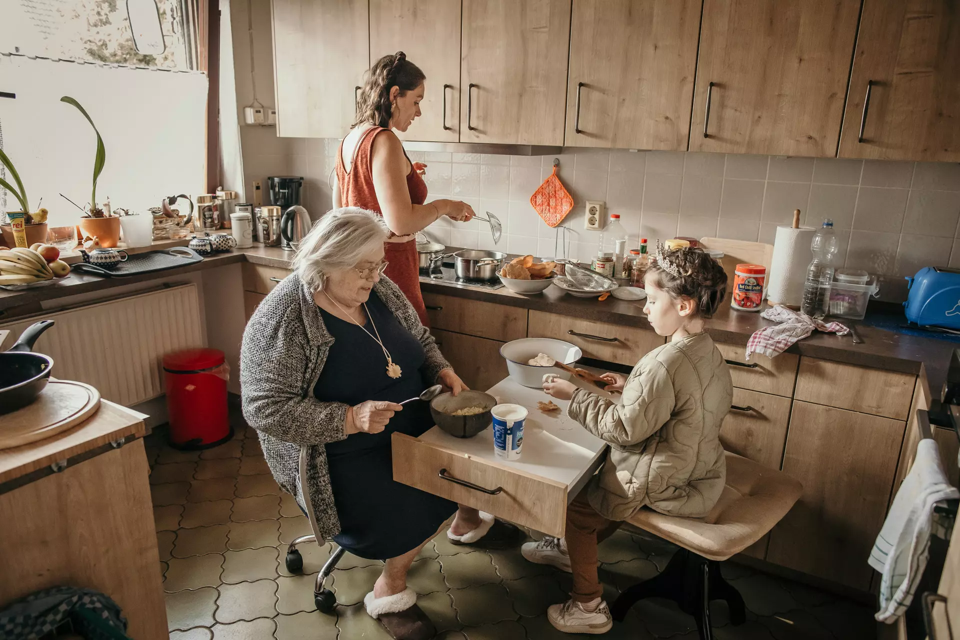 Gro&szlig;elternfotoshooting - ungestellte Familienfotos im Wohnzimmer und K&uuml;che - Drei Generationen bereiten gemeinsam das Abendessen in einer Berliner Wohnung vor: Oma, Enkelin und Urenkelin