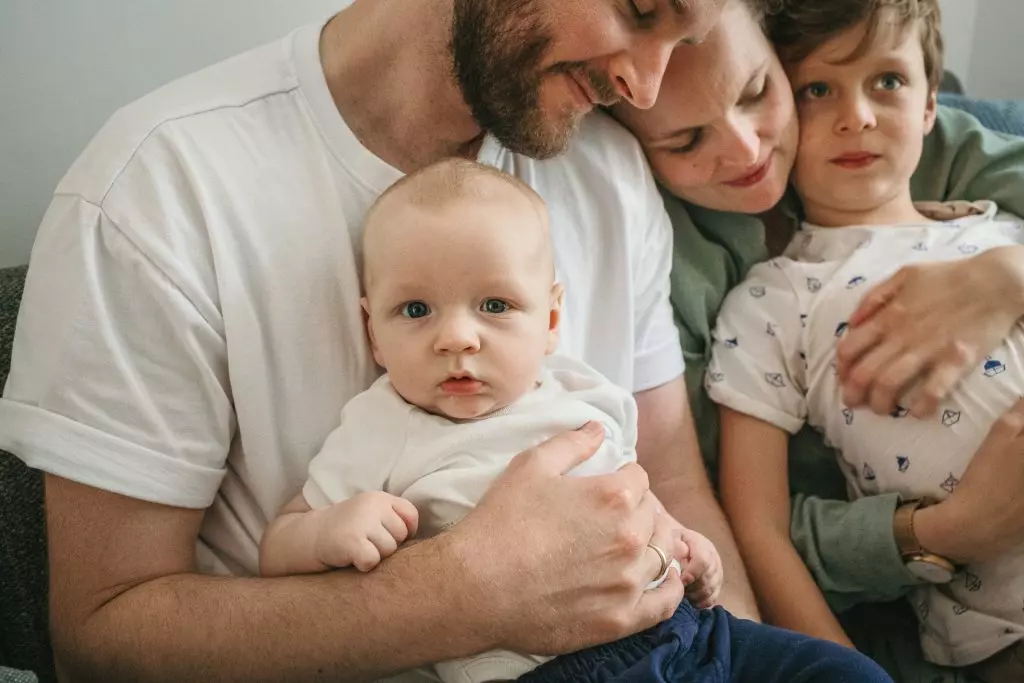Babyfotoshooting - Ein Baby sitzt bei seinem Papa auf dem Scho&szlig; und schaut in die Kamera