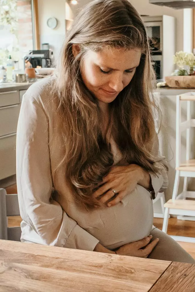 Schwangere Frau l&auml;chelt und h&auml;lt liebevoll ihren Babybauch
