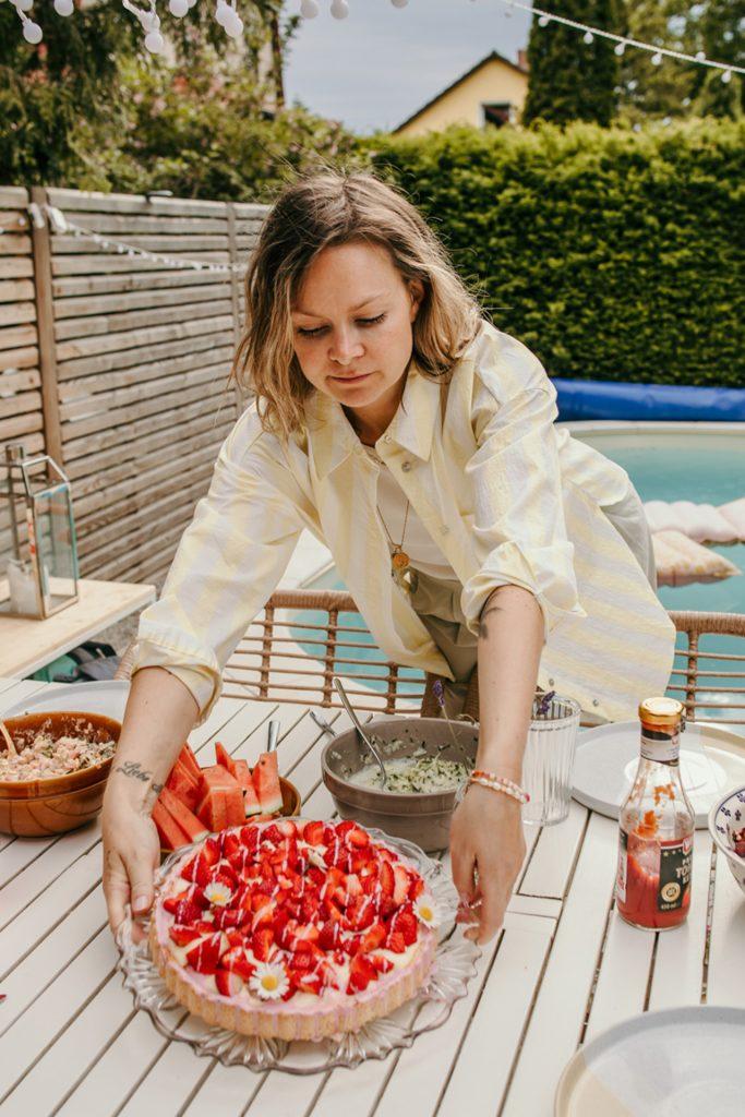 Frau stellt selbstgebackenen Erdbeerkuchen auf den Gartentisch