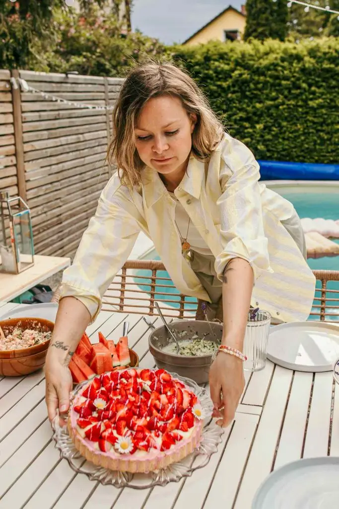 Mama stellt die Erdbeertorte auf den Gartentisch, Hochformat, Familienalltag