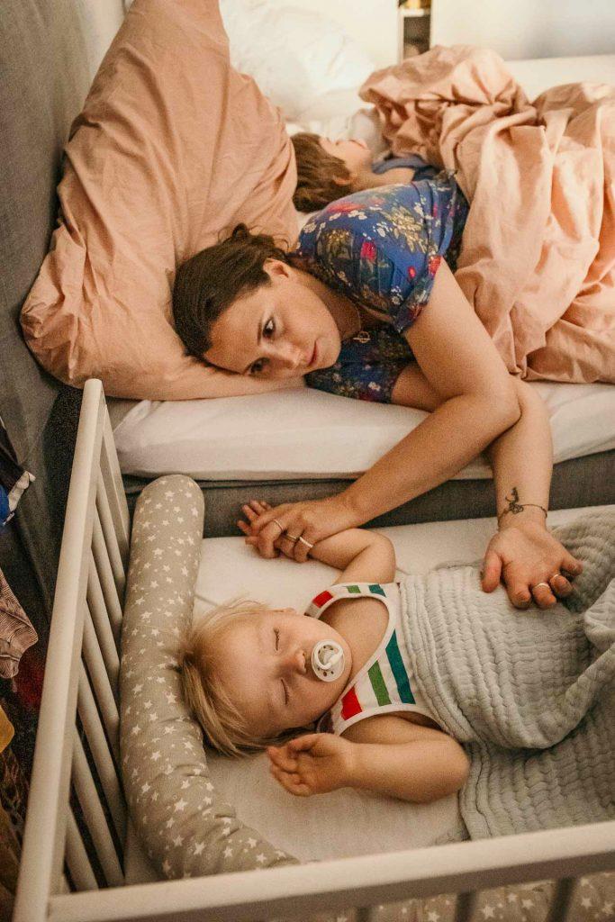 Familienreportage Berlin Prenzlauer Berg, Mama liegt neben dem schlafenden Sohn und hält seine Hand, großer Bruder schläft